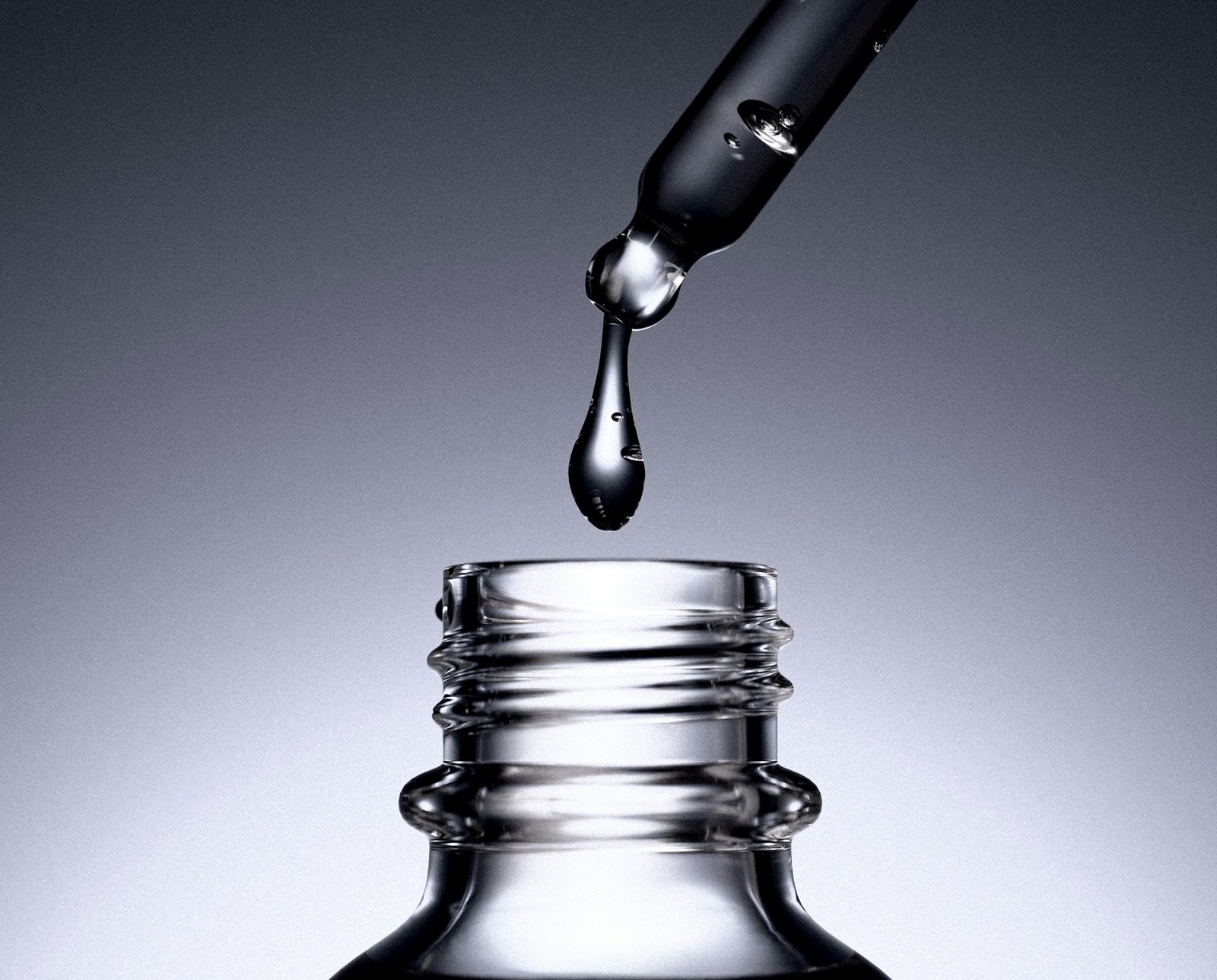 A drop of serum falling from a glass dropper into a bottle