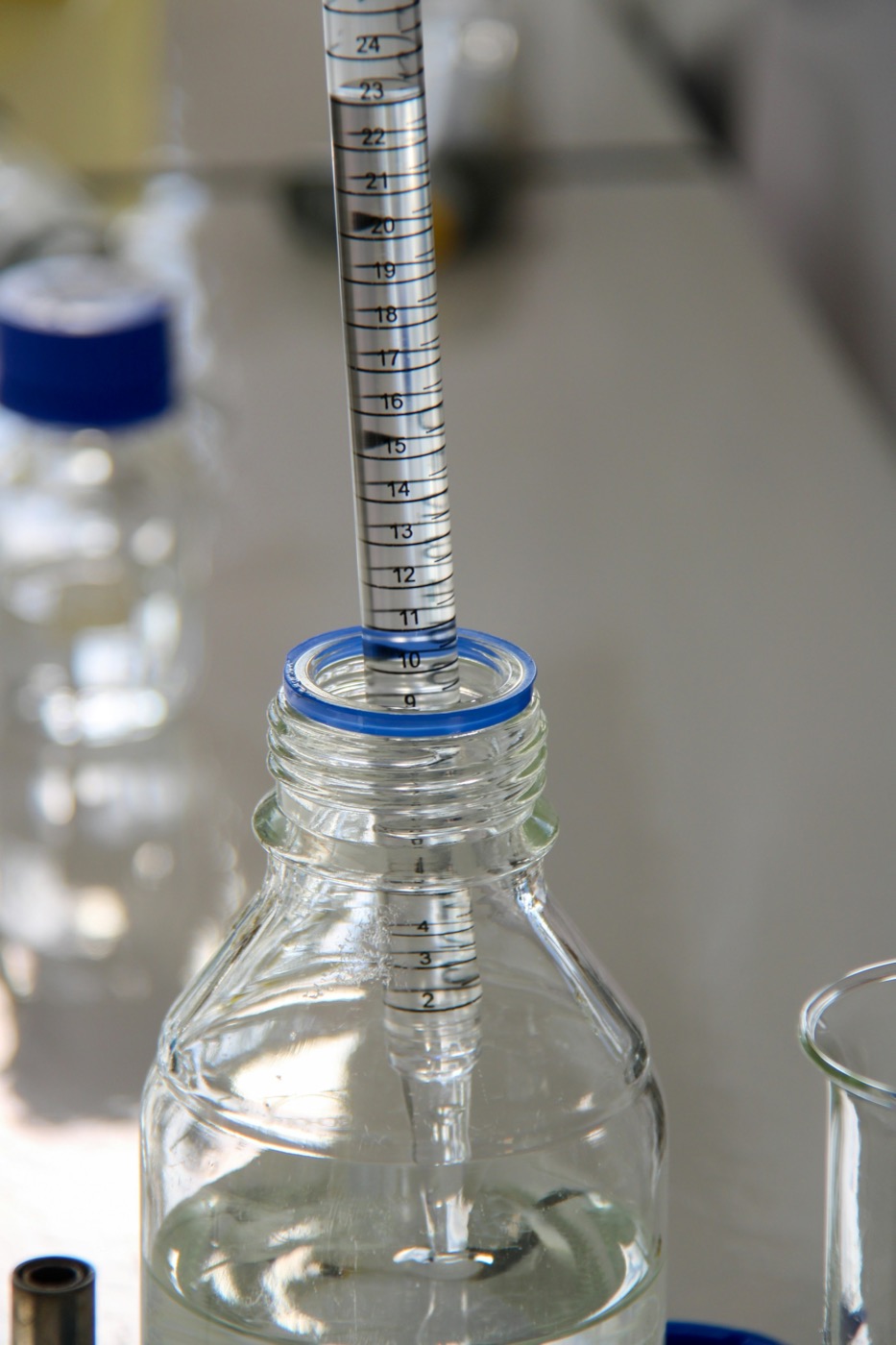 A graduated pipette dispensing liquid into a glass lab bottle